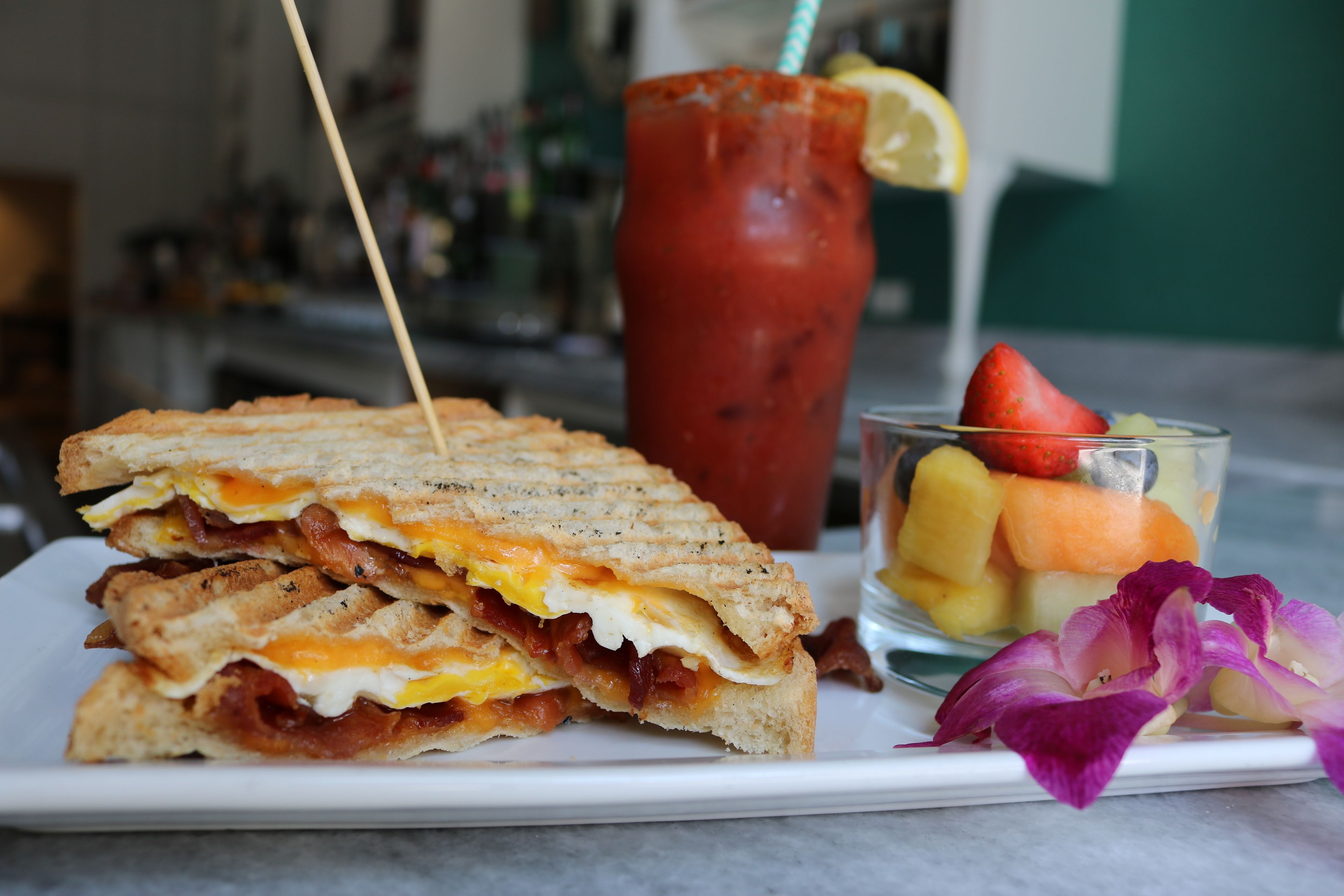 Un sándwich de huevo y tocino, un vaso de fruta y una bebida con pajita.