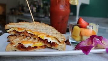 Un sándwich de huevo y tocino, un vaso de fruta y una bebida con pajita.