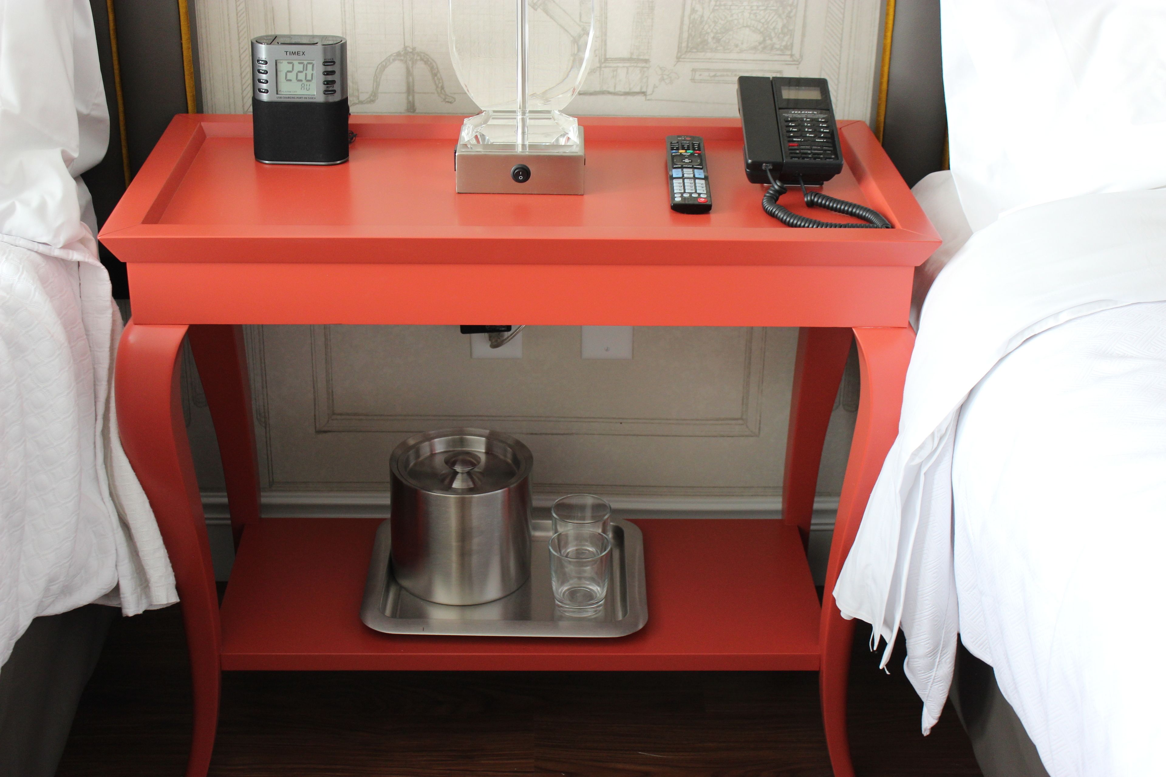 A red hotel desk with a coffee maker, two glasses, a remote control, and a phone.