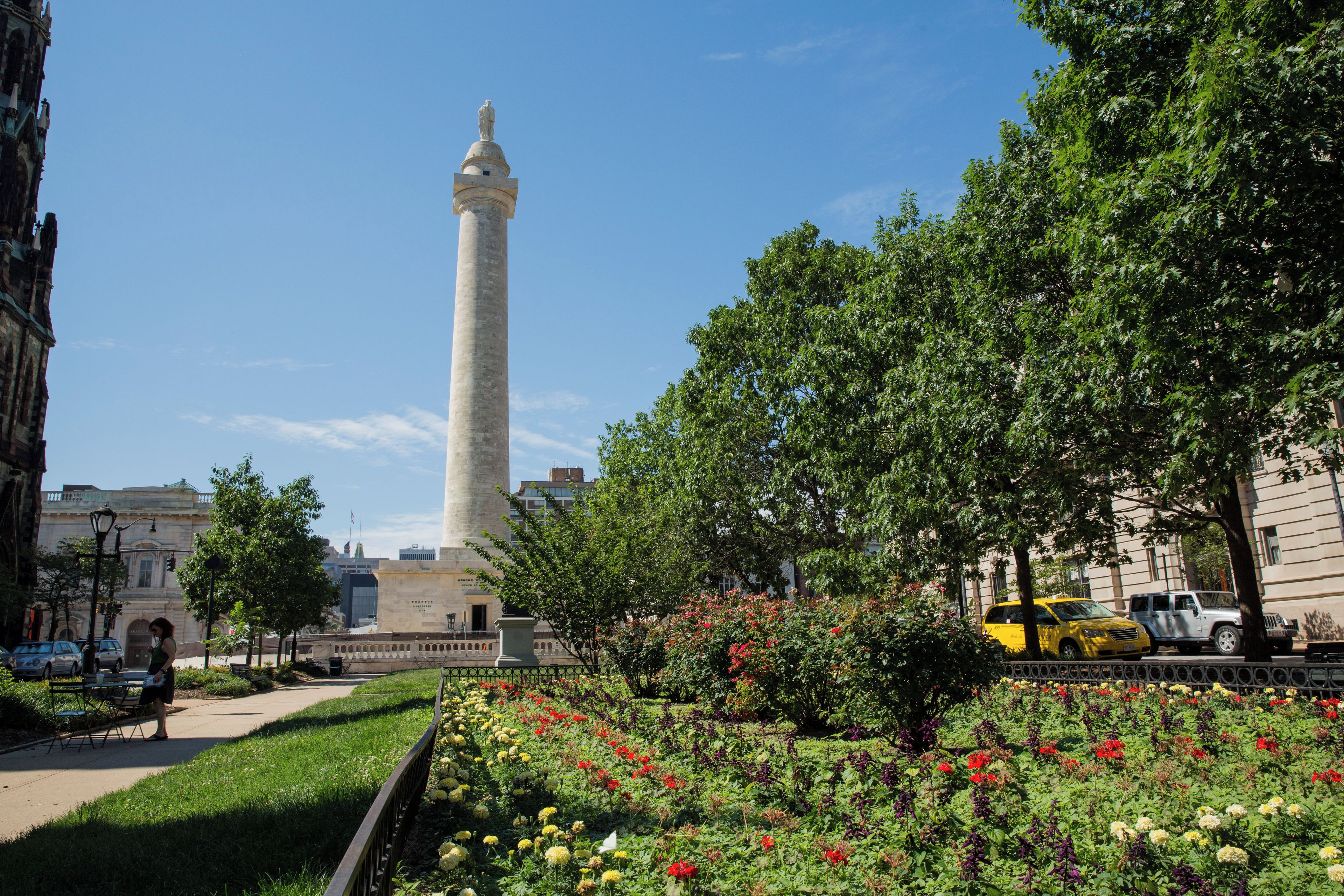 A tall monument with a statue on top, surrounded by a well-maintained garden with various flowers and trees.