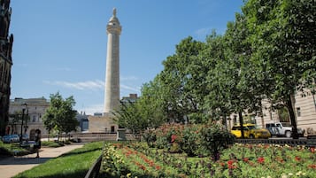 Un monumento alto con una estatua en la cima, rodeado de un jardín bien cuidado con diversas flores y árboles.