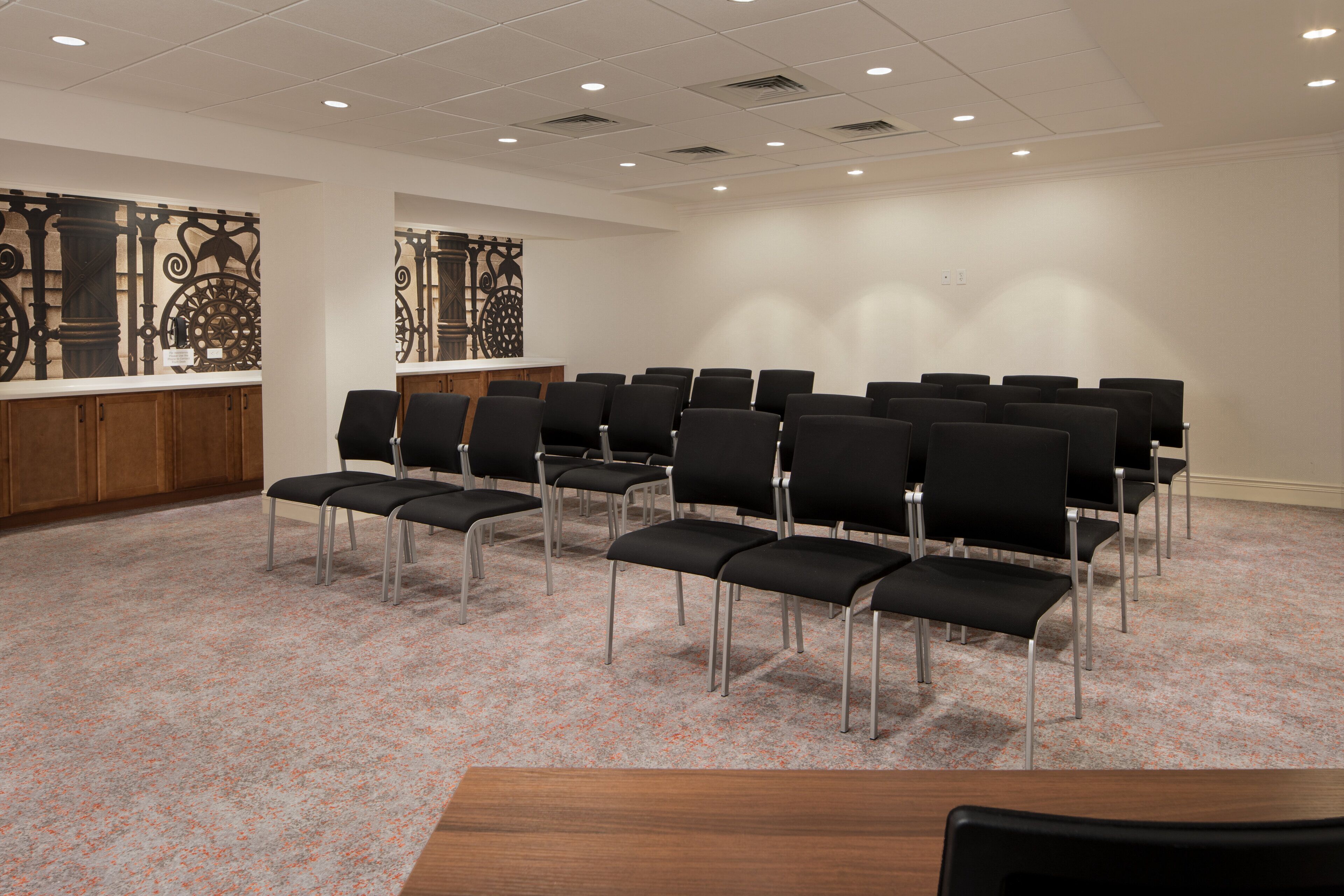 A conference room with rows of black chairs, a wooden podium, and decorative wall panels.