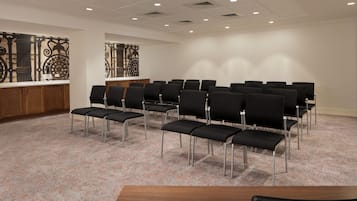 A conference room with rows of black chairs, a wooden podium, and decorative wall panels.