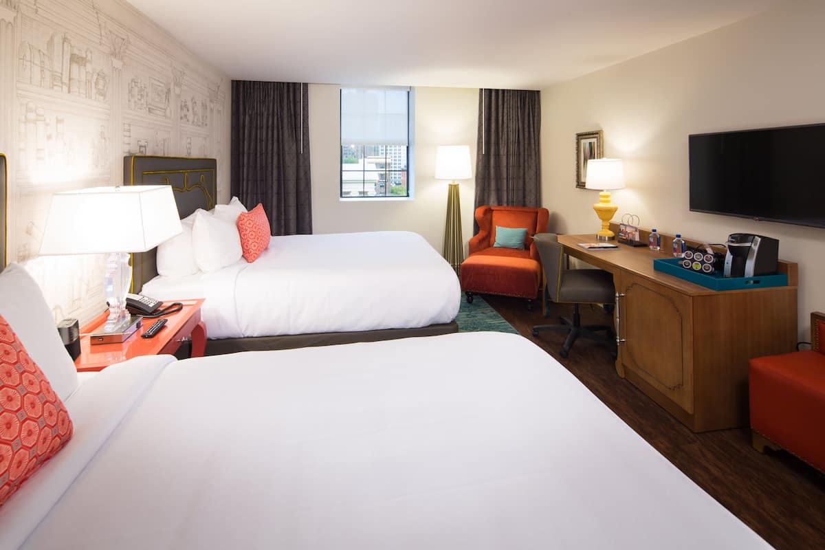 Une chambre d’hôtel avec deux lits, un bureau, une chaise, une télévision et une fenêtre donnant sur la ville.