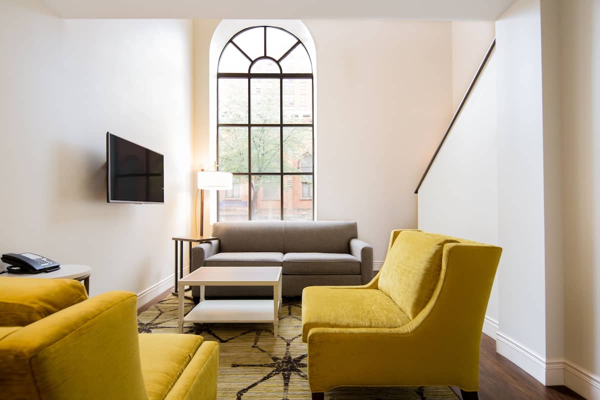 Un salon moderne doté d’une grande fenêtre, d’un canapé, de deux fauteuils jaunes, d’une table basse et d’un téléviseur à écran plat.