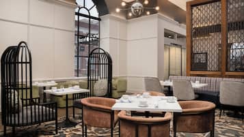 A hotel dining area with tables set for service, cushioned seating, and a decorative wall with geometric patterns.