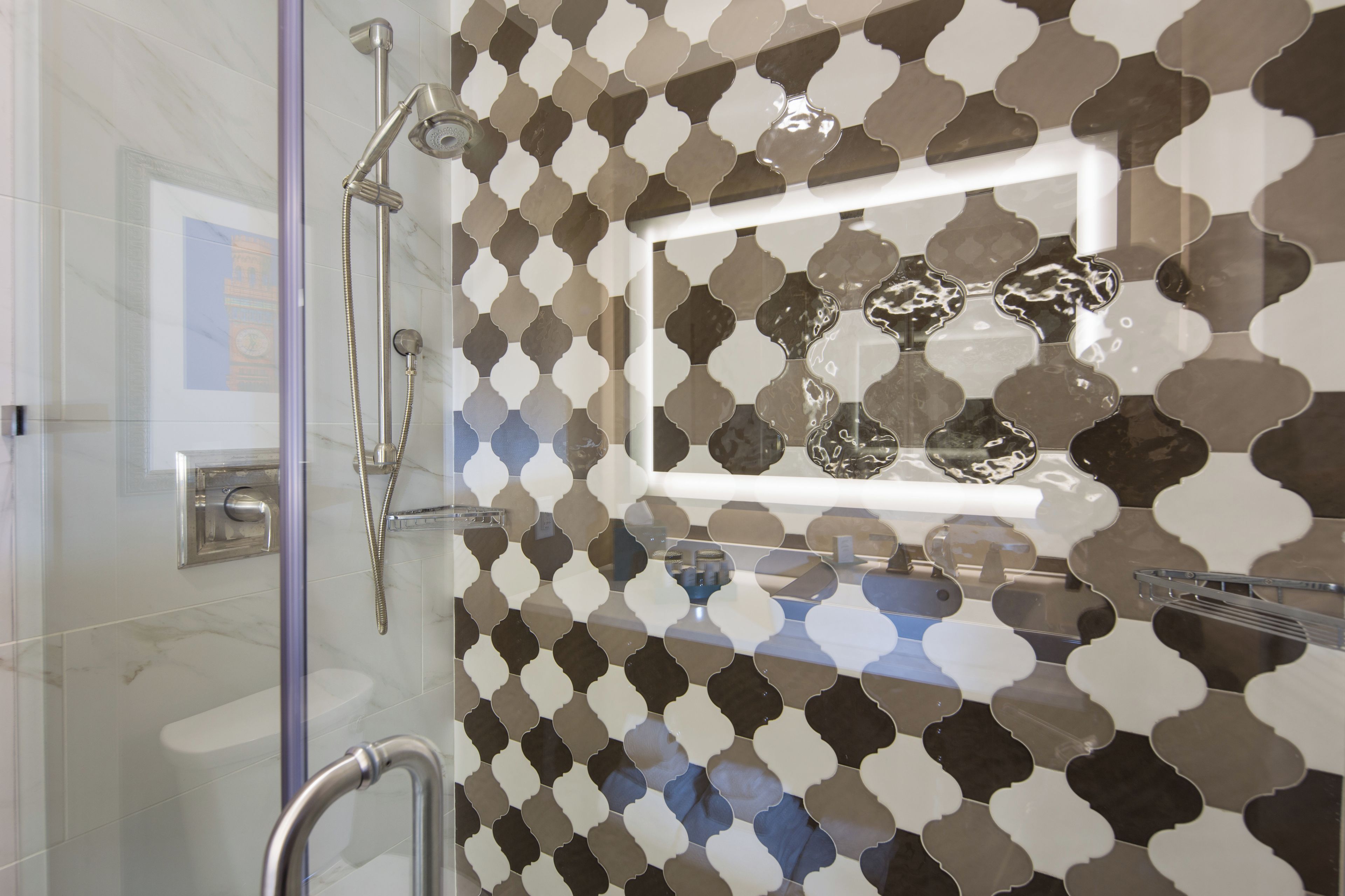 Une salle de bain dotée d’une douche à parois de verre, d’une barre d’appui et d’un mur recouvert de carreaux décoratifs.
