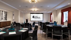 A conference room with round tables, black chairs, and a projector screen displaying the hotel name. - Hotel Indigo Baltimore Downtown by IHG (Baltimore)