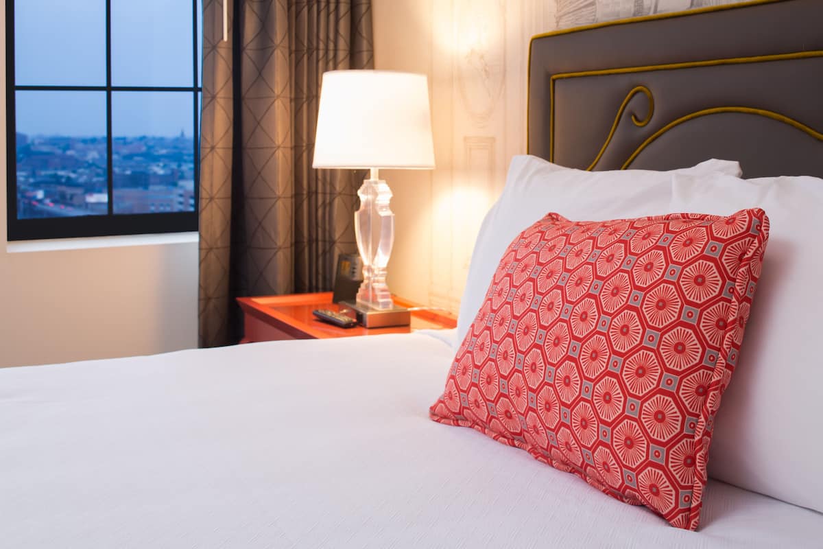 Une chambre d’hôtel avec un lit, une table de chevet avec une lampe et une vue sur la ville par la fenêtre.