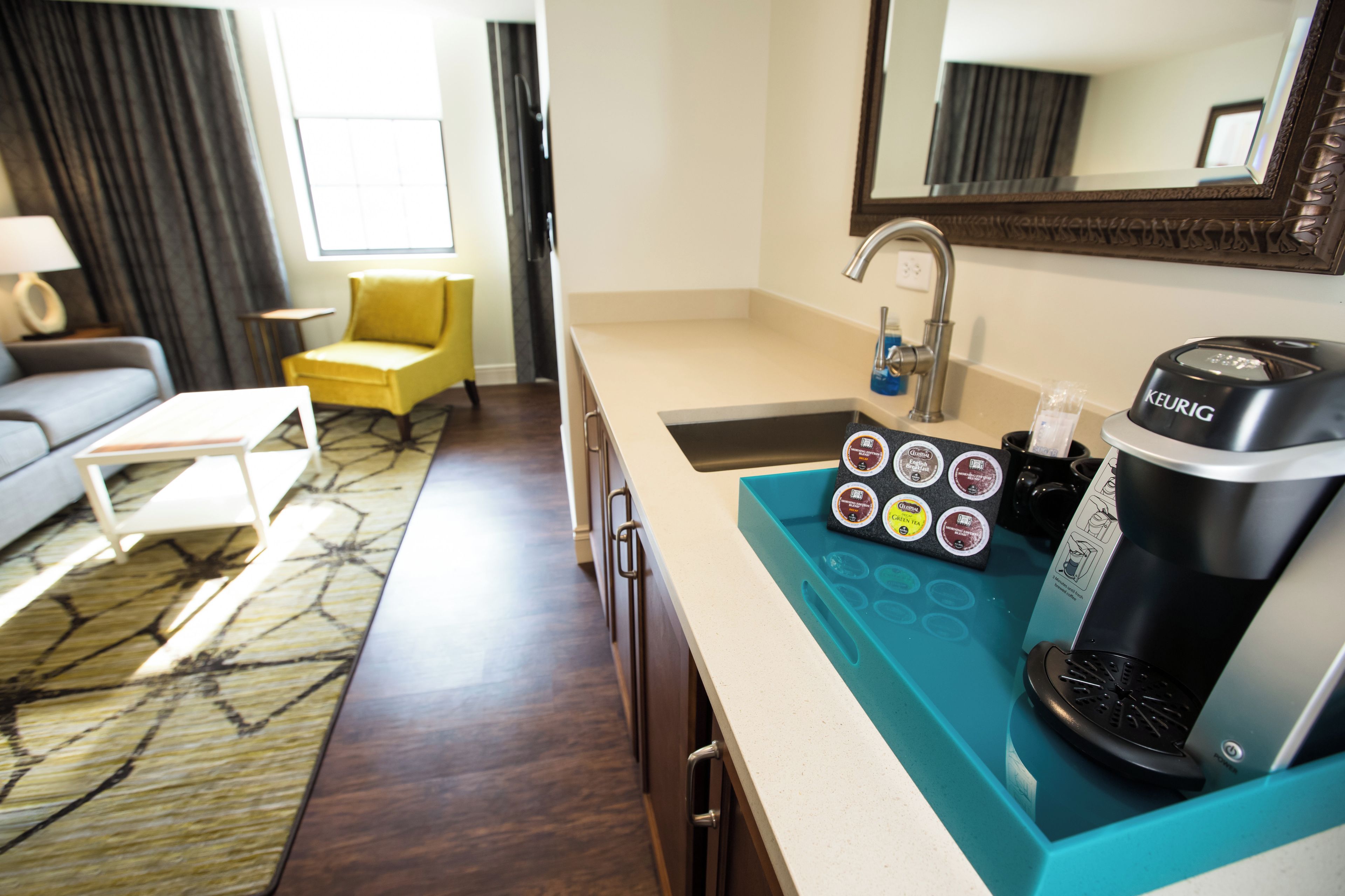 A hotel room with a kitchenette, a coffee maker, and a coffee pod holder.