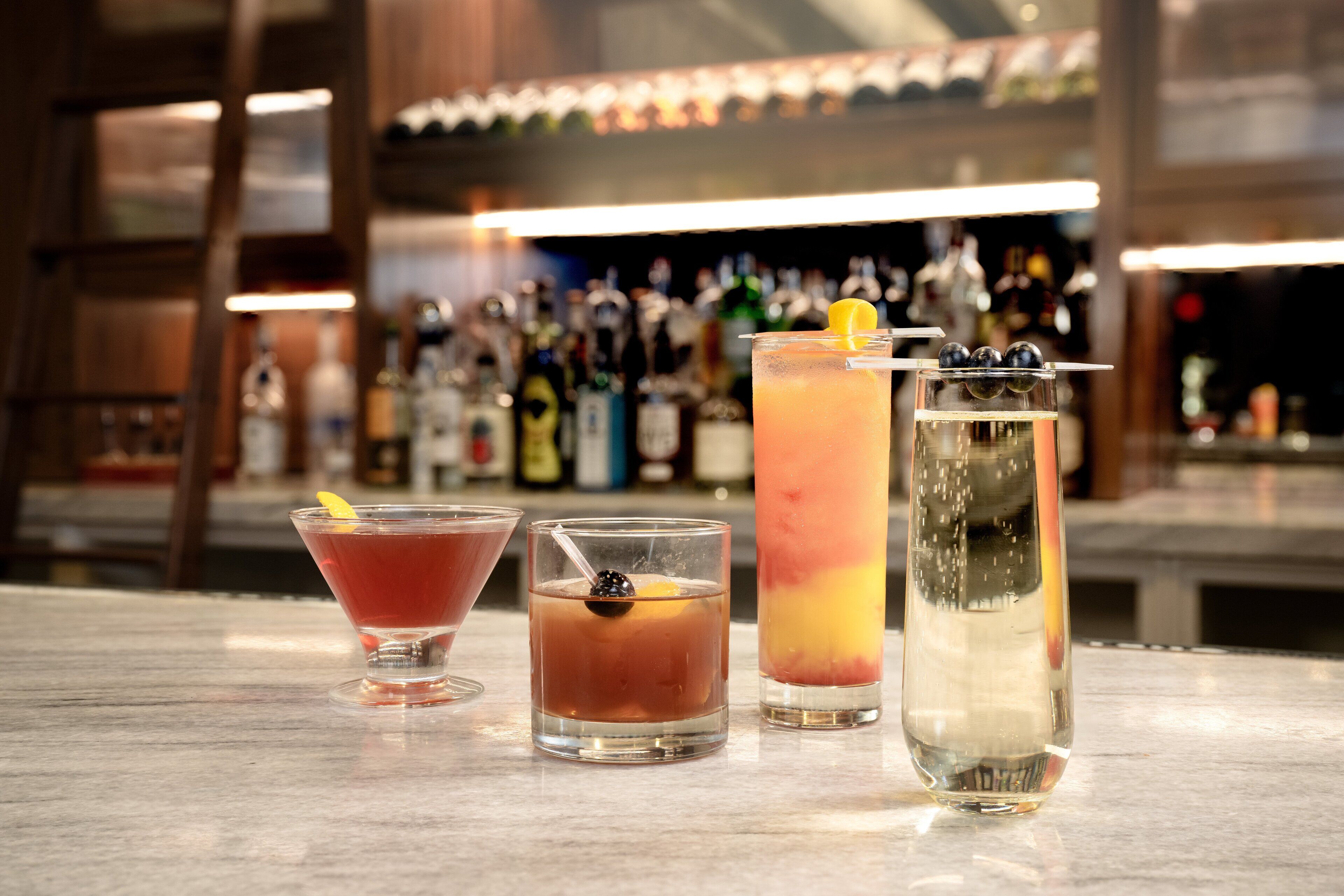 Drei Cocktails auf einer Bar, im Hintergrund verschwommen Flaschen.