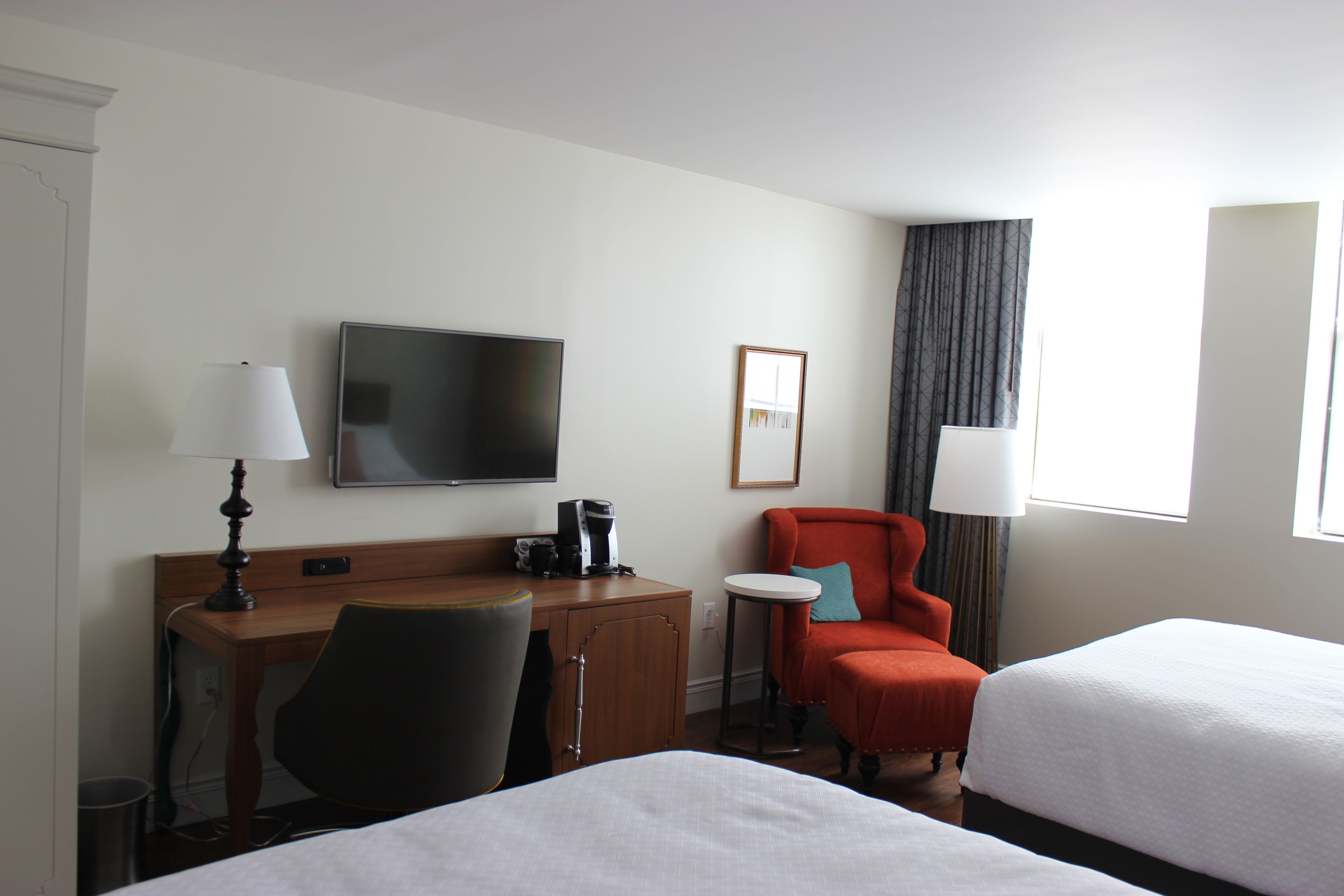 Habitación de hotel con escritorio, silla, televisor, dos camas y ventana con cortinas.
