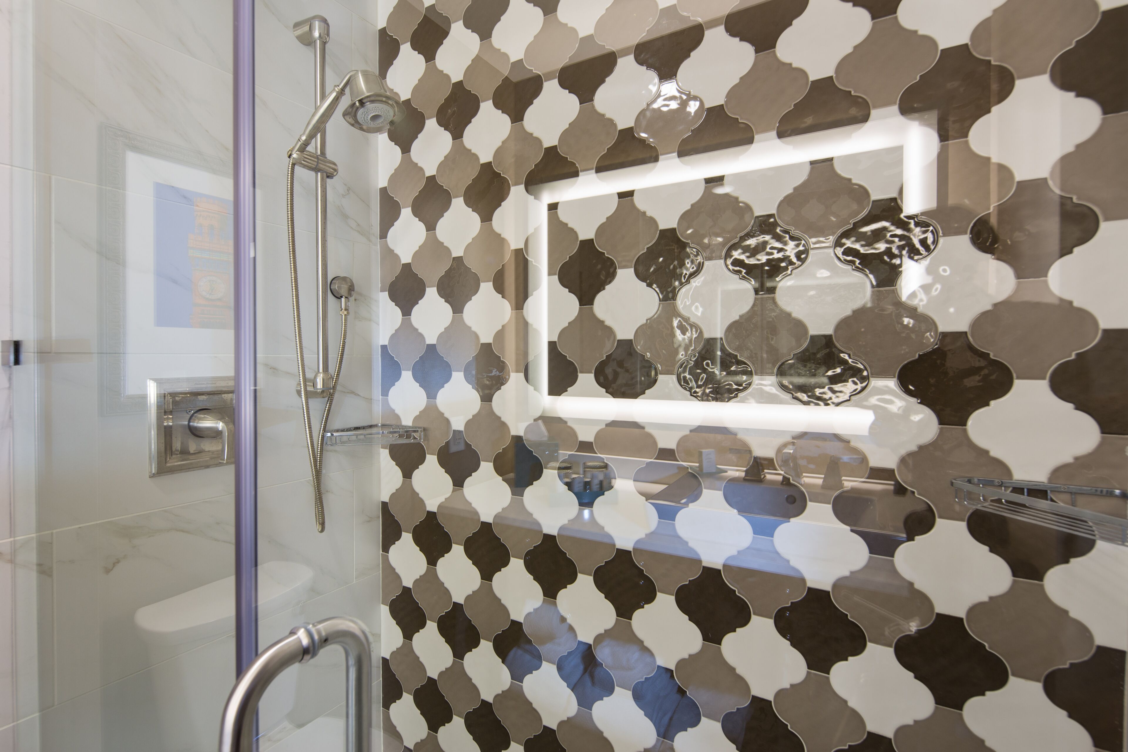 Un baño moderno con cabina de ducha de vidrio, barra de apoyo y salpicadero de azulejos estampados.