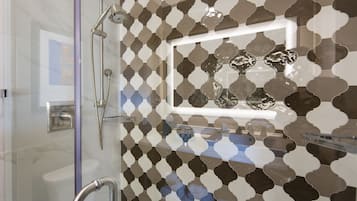 Un baño moderno con cabina de ducha de vidrio, barra de apoyo y salpicadero de azulejos estampados.