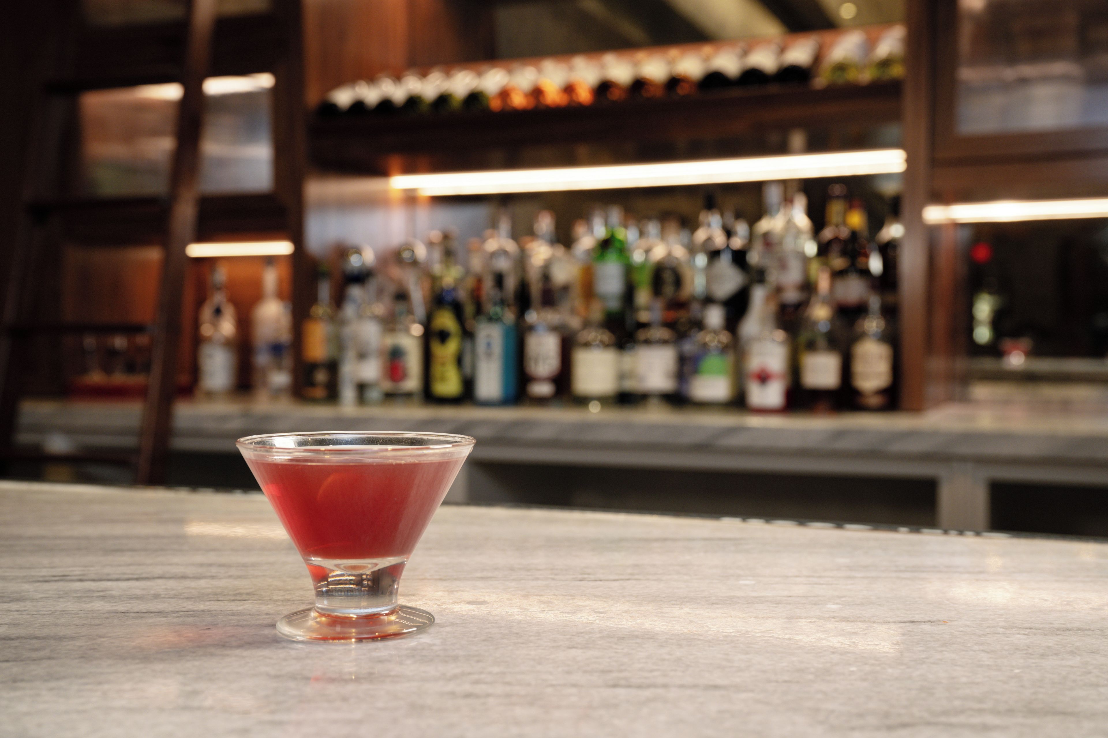 Um copo de martini com uma bebida vermelha sobre um balcão de bar.