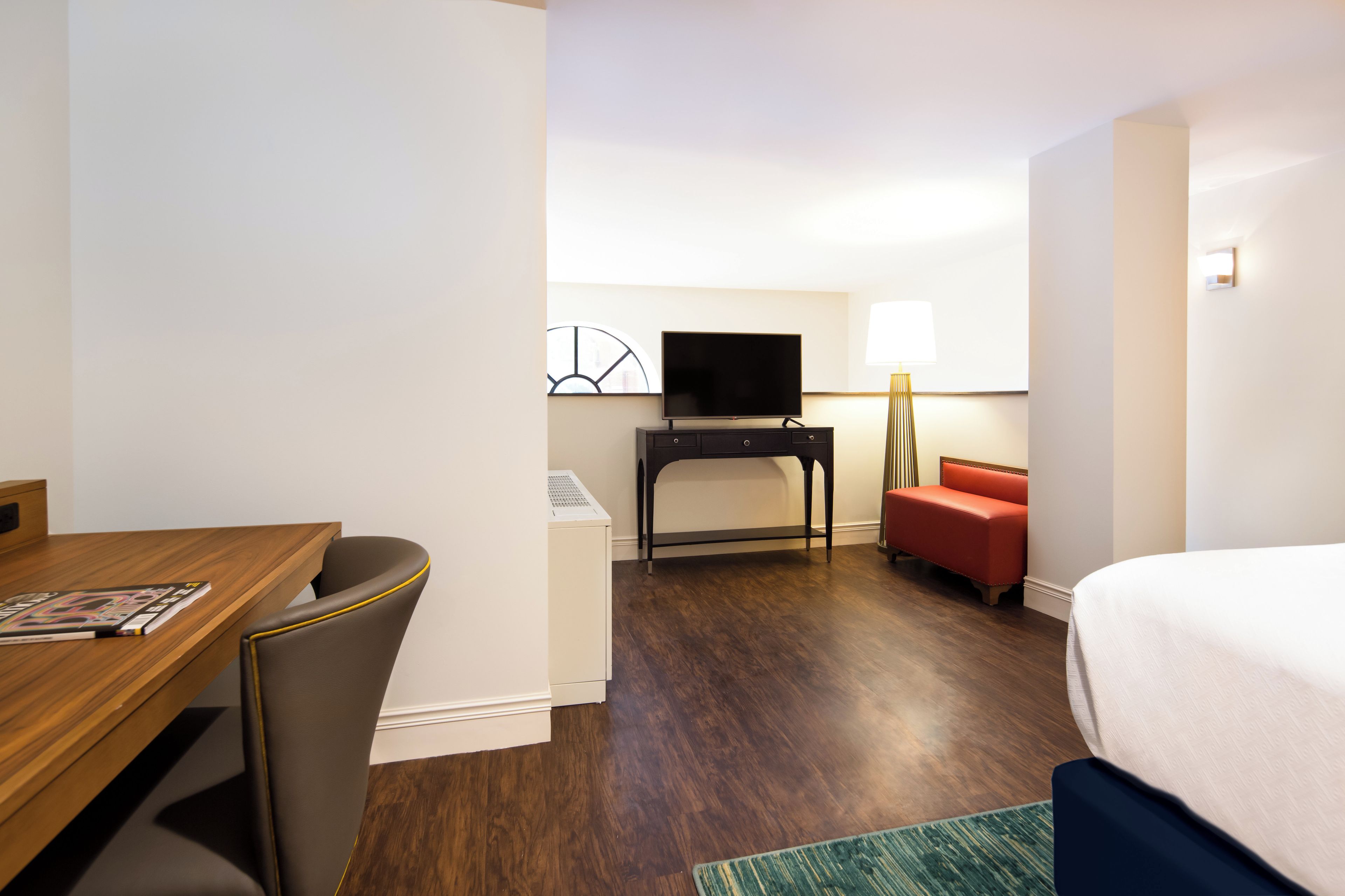 Habitación de hotel con un escritorio de madera, un televisor sobre un mueble bajo, un sofá rojo y una cama.