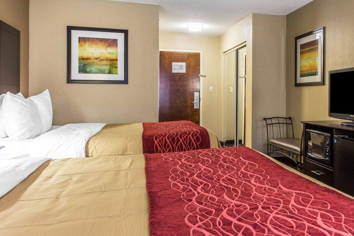 A hotel room with two beds, a TV, a desk, and a door leading to another room.