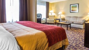 Een hotelkamer met een groot bed, twee fauteuils, een bank en een bureau. Er staan twee lampen op het bureau en er hangt een schilderij aan de muur.