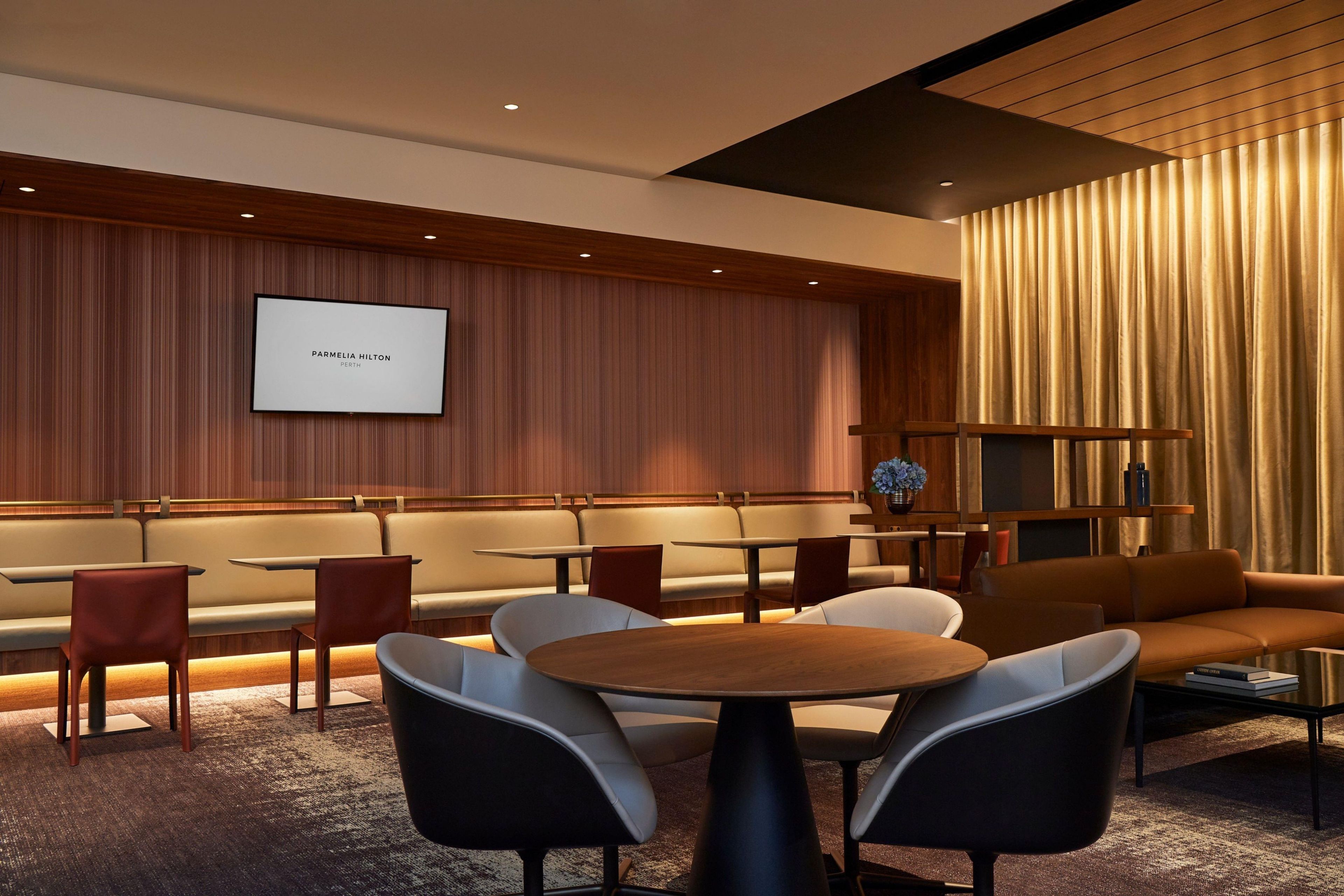 A modern lounge area with seating arrangements, a projection screen, and a decorative wall.