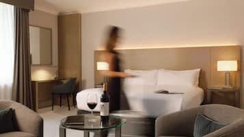 Una habitación de hotel con una cama, dos lámparas de noche, una mesita de cristal con una botella de vino y una copa, una silla y un escritorio con una silla.