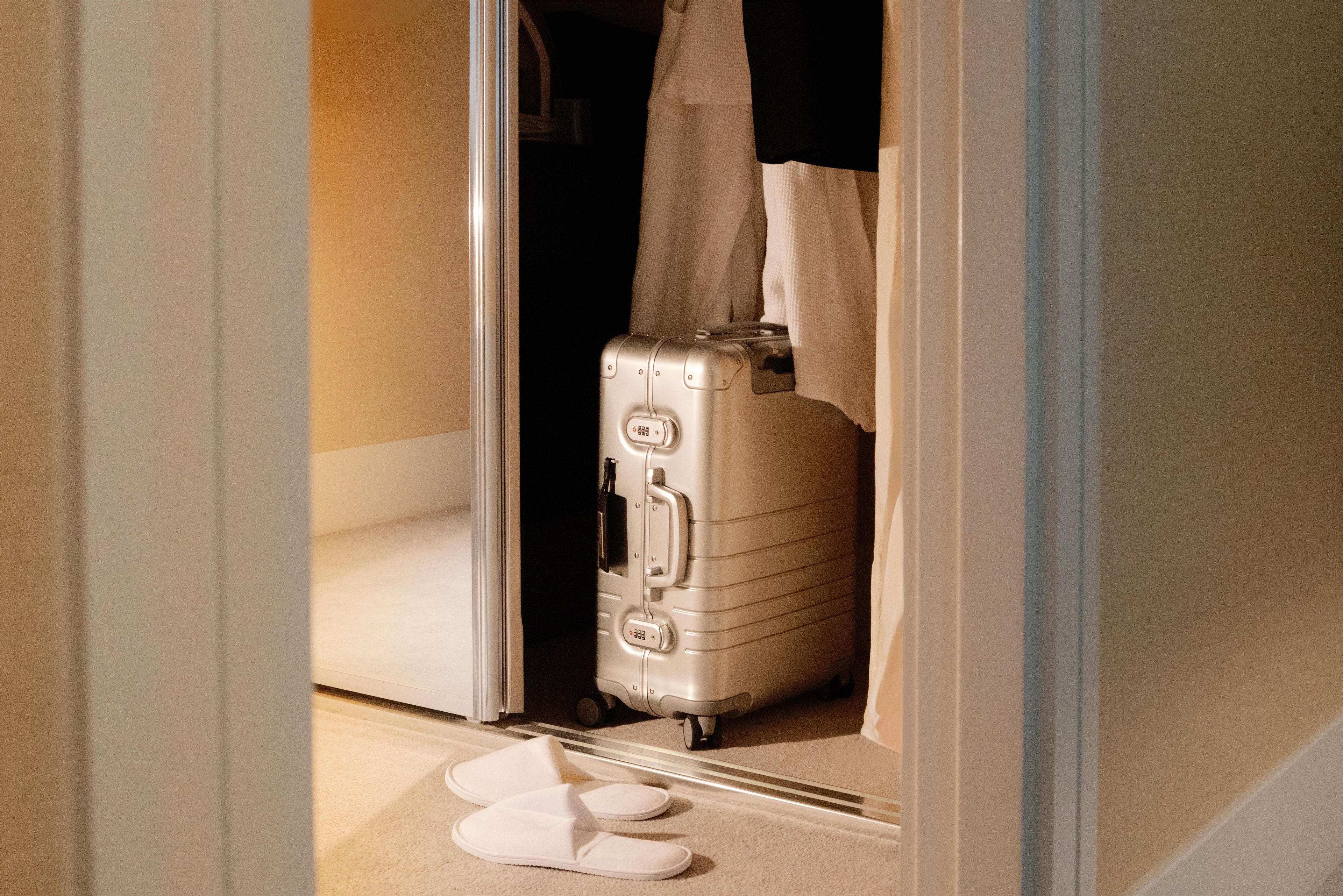 A room with a suitcase and slippers on the floor, a door, and a towel hanging on the door.