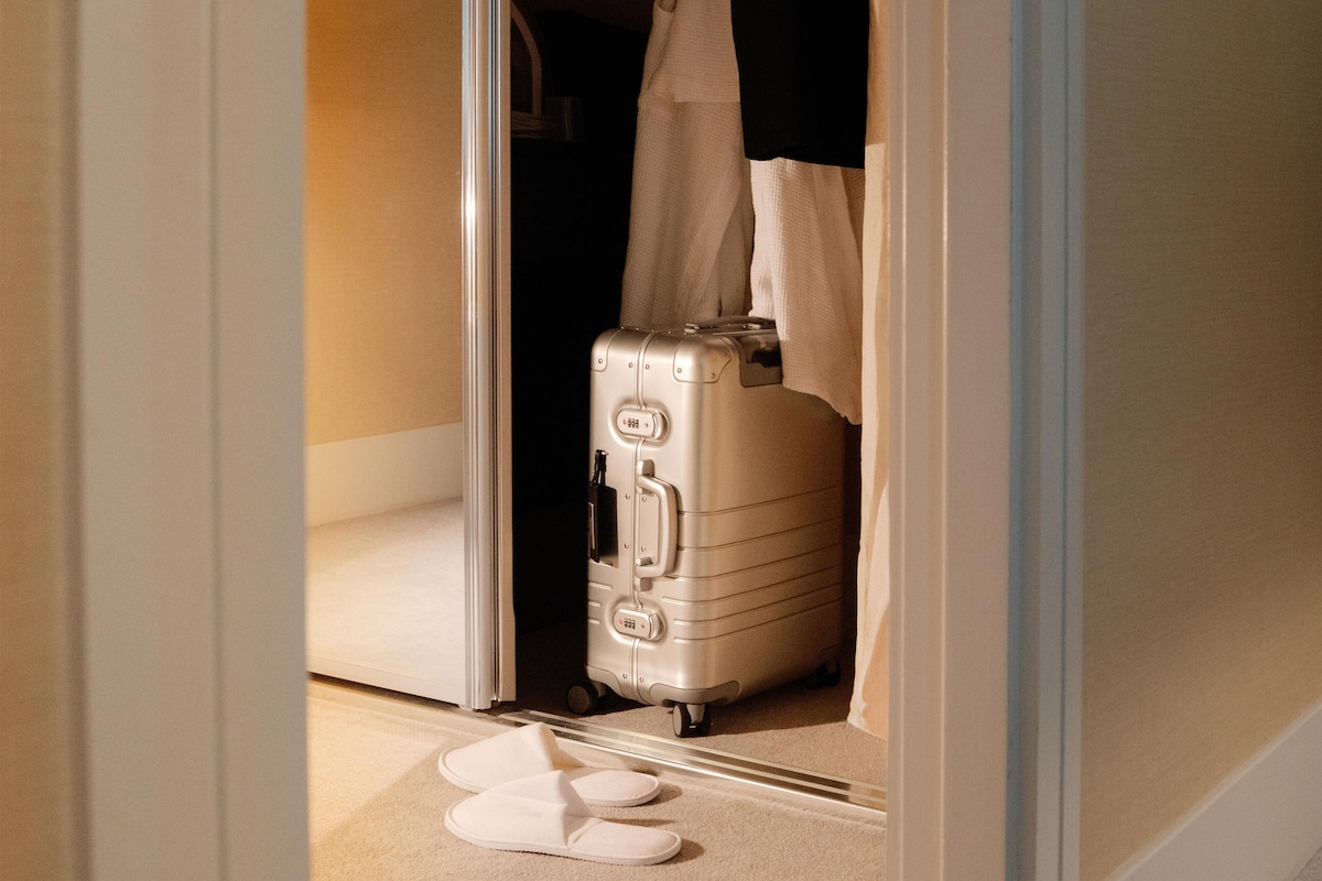 A room with a suitcase and slippers on the floor, a door, and a towel hanging on the door.