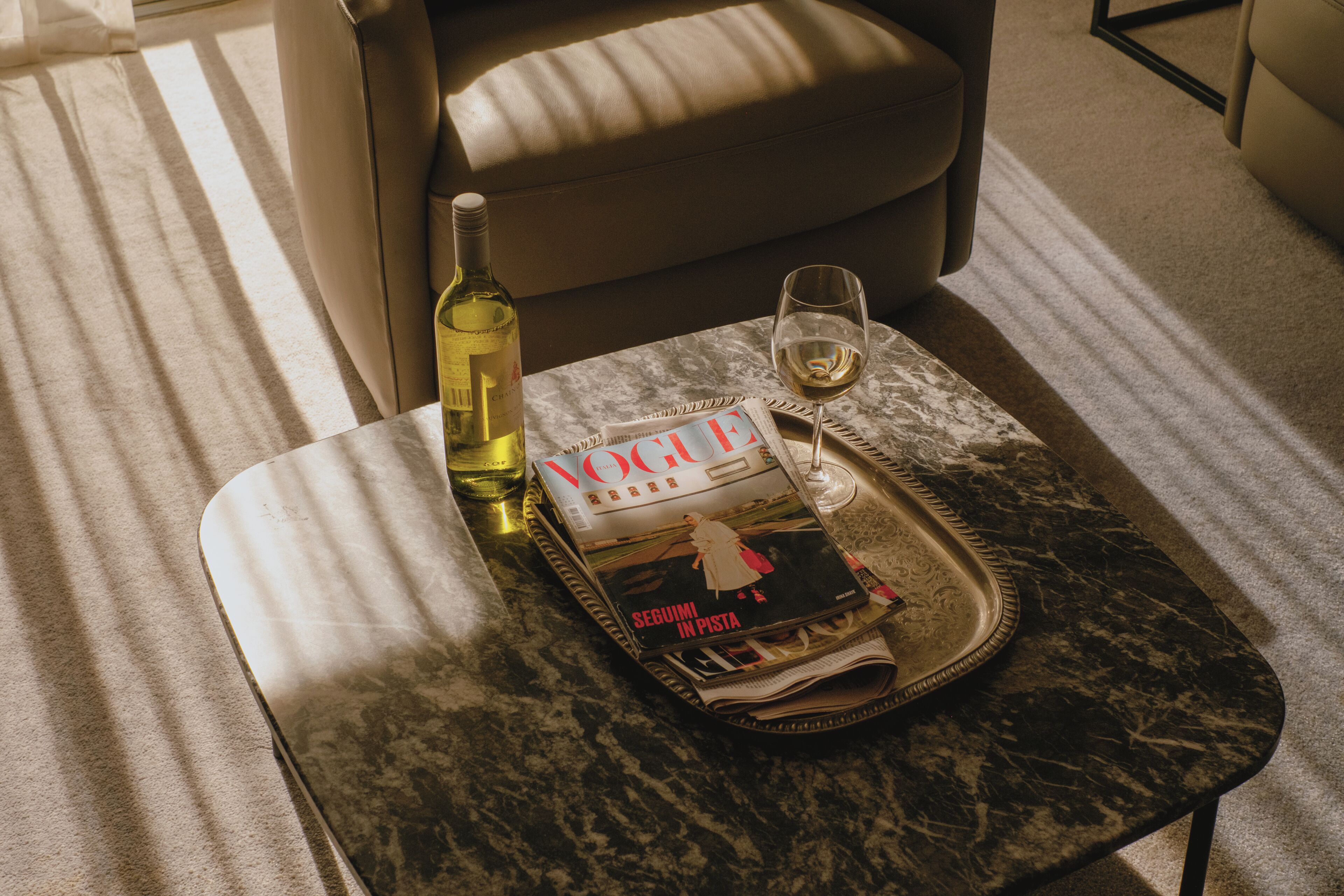A magazine, a bottle, and a glass on a tray on a marble table.