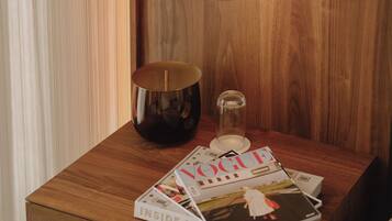 A wooden bedside table with a lamp, a candle, and magazines.