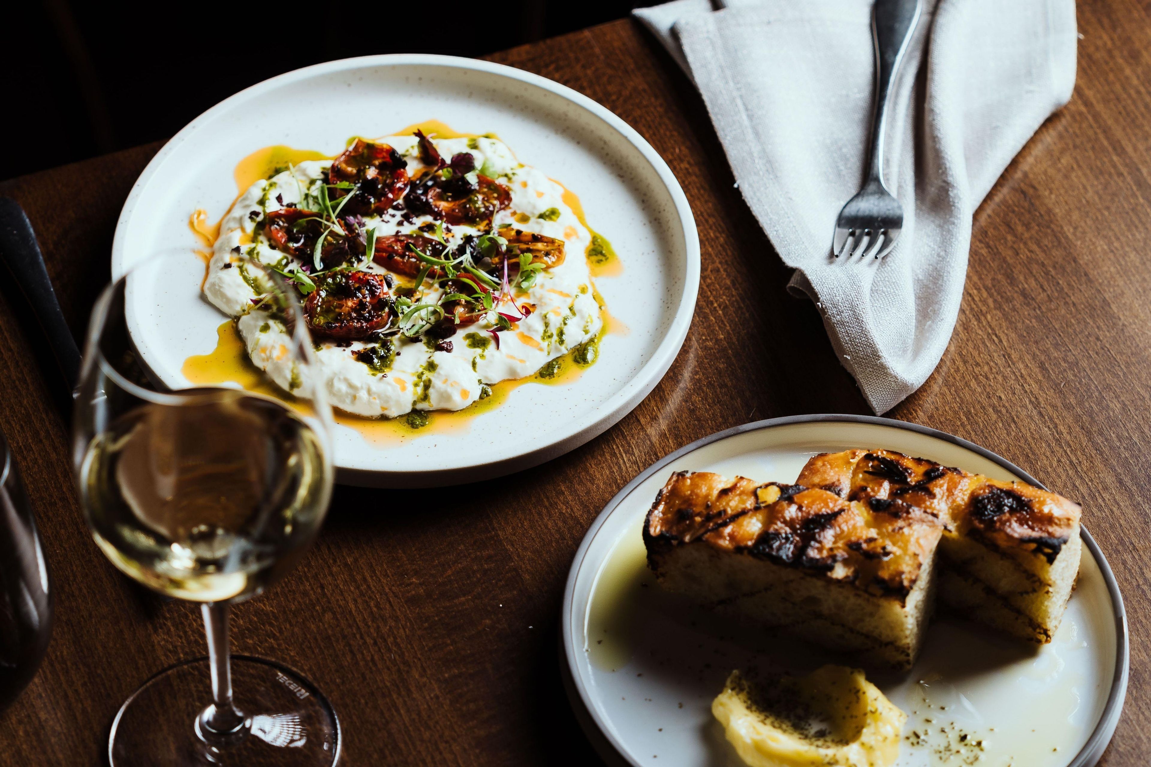 A plate of food with a fork and a glass of white wine on a wooden table.