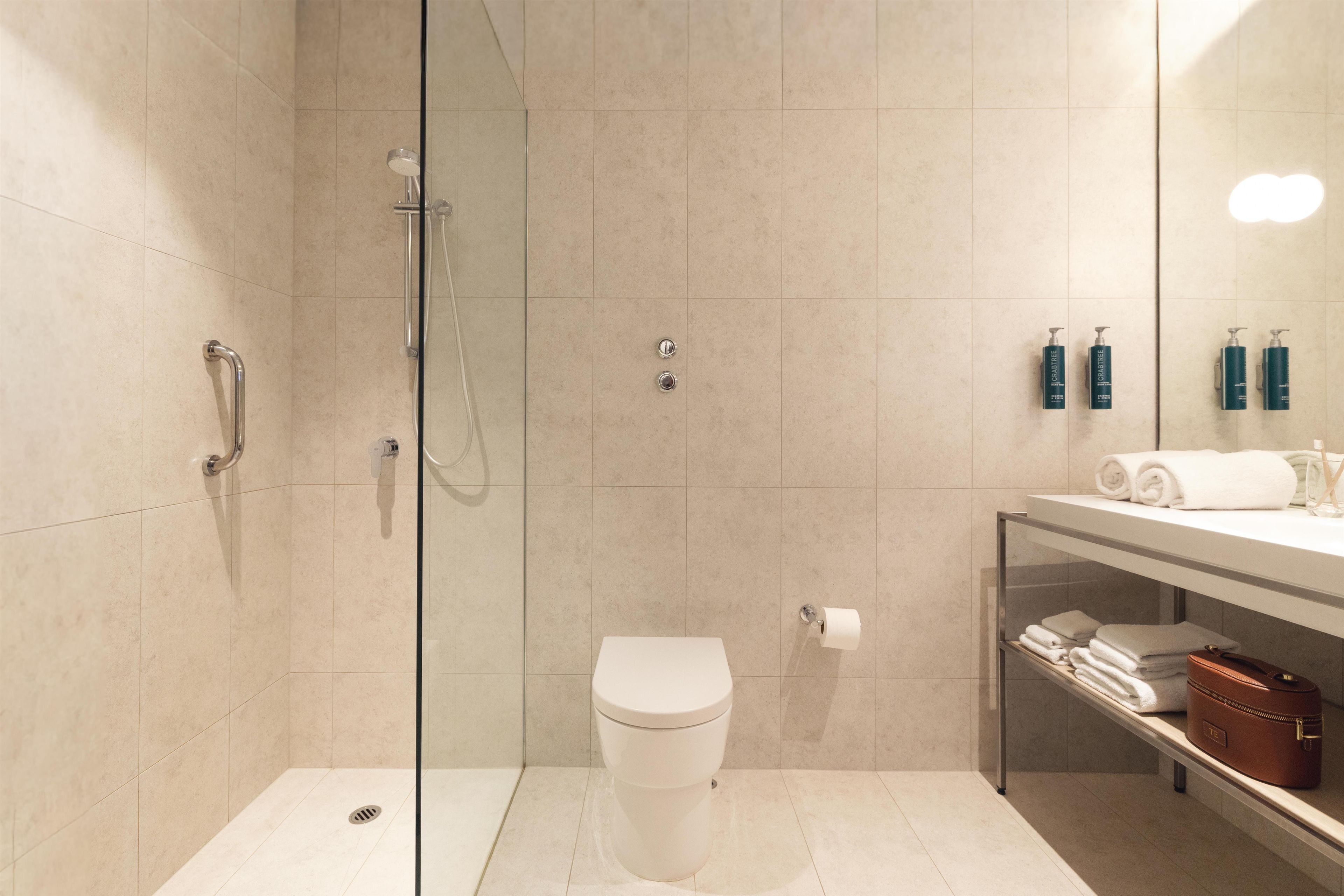 A modern bathroom with a glass-enclosed shower, a toilet, and a vanity with toiletries.