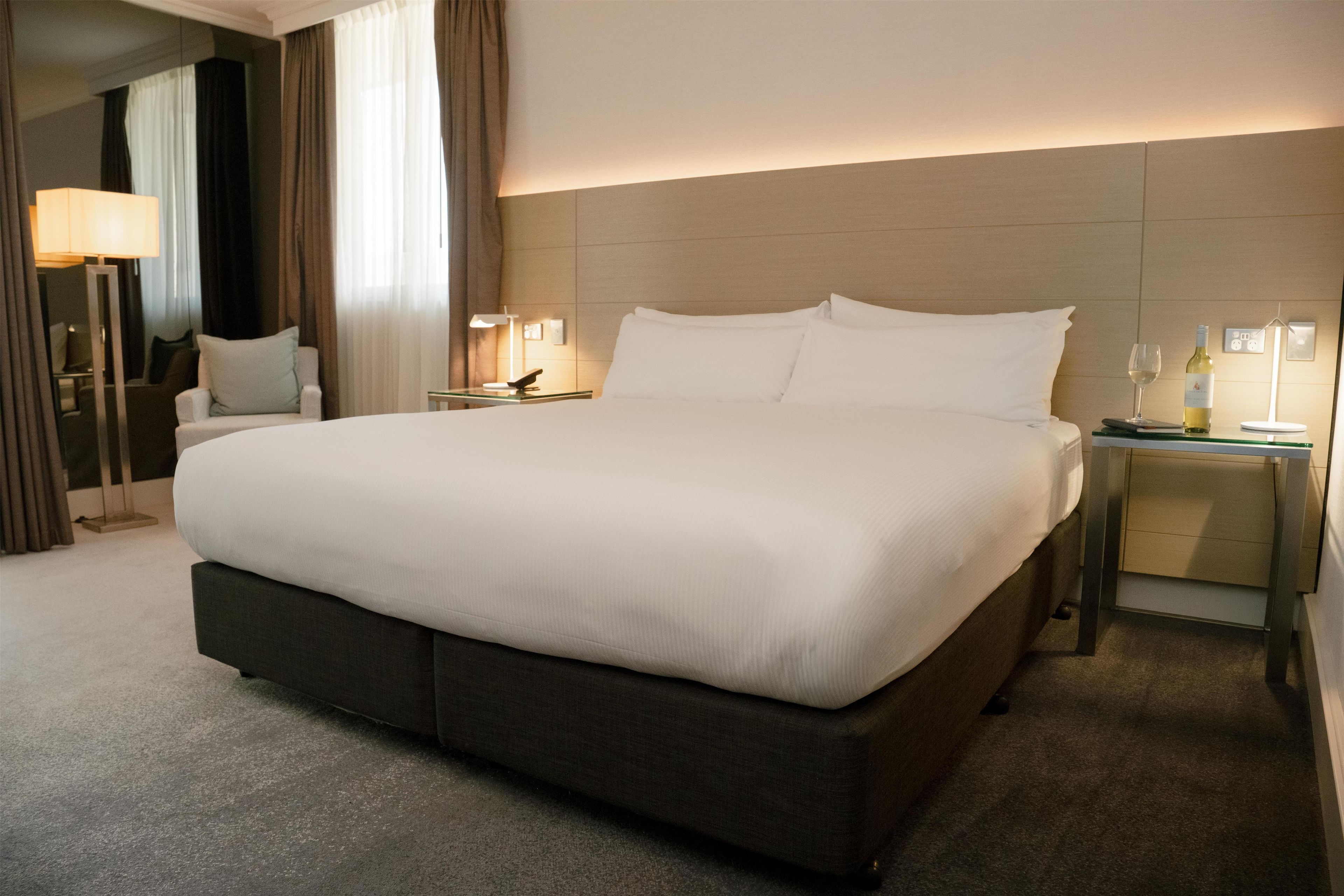 A hotel room with a large bed, bedside tables, a lamp, and a wine bottle.