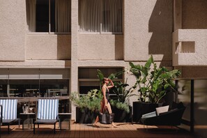 A woman in a swimsuit walking on a wooden deck with outdoor seating and potted plants. - Parmelia Hilton Perth (Perth)