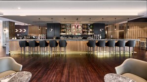 A modern bar area with a long counter, multiple bar stools, and a variety of bottles and glasses. - Parmelia Hilton Perth (Perth)
