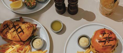 A table with four plates of food, including fish and burgers, accompanied by sides of fries and condiments.