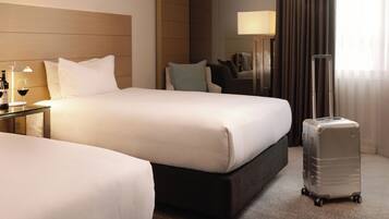 Een hotelkamer met twee bedden, een nachtkastje met een lamp, een koffer en uitzicht op het omliggende landschap.