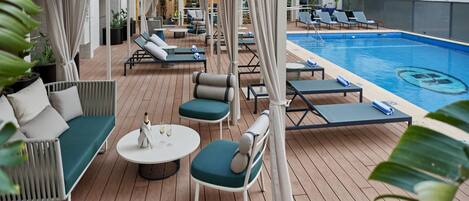 Un espace aménagé au bord de la piscine, avec des chaises longues, un canapé et une petite table.