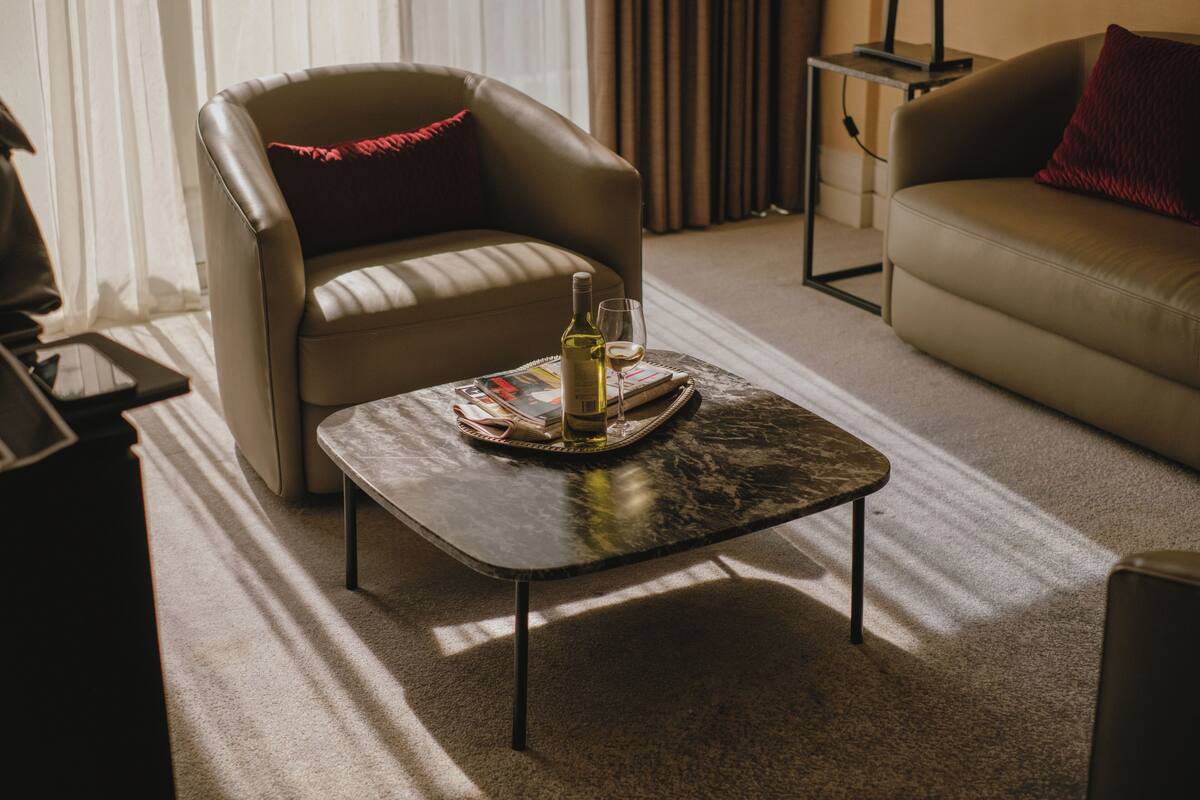 A modern living room with a leather sofa, a leather armchair, a marble coffee table with a bottle and glass, and a small side table.