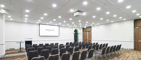 A conference room with rows of chairs, a projector screen, and a carpeted floor.