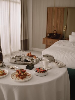 A hotel room with a neatly arranged breakfast table, a bed, a wooden nightstand, and a mirror.