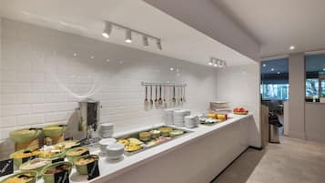 Un buffet proposant divers plats et ustensiles, une machine à café et un grand récipient isotherme pour le café.