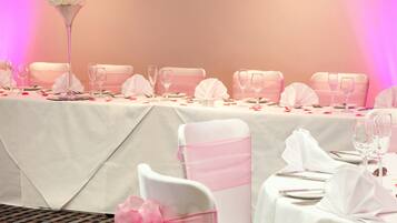 A banquet table set for a formal event with white tablecloths, pink sashes, and clear glassware.