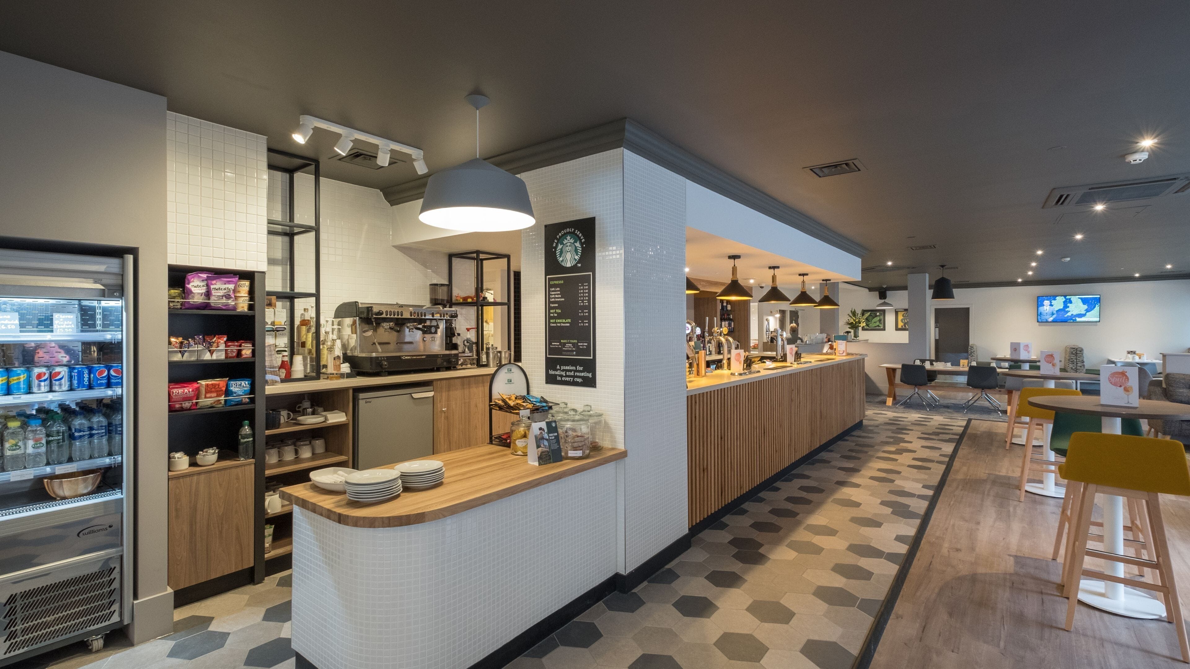 Ein modernes Café mit einer Kaffeemaschine, einer Speisekarte und Sitzbereichen.
