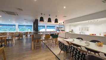 Un comedor moderno con mesas y sillas de madera, iluminación colgante y vistas al exterior a través de amplios ventanales.