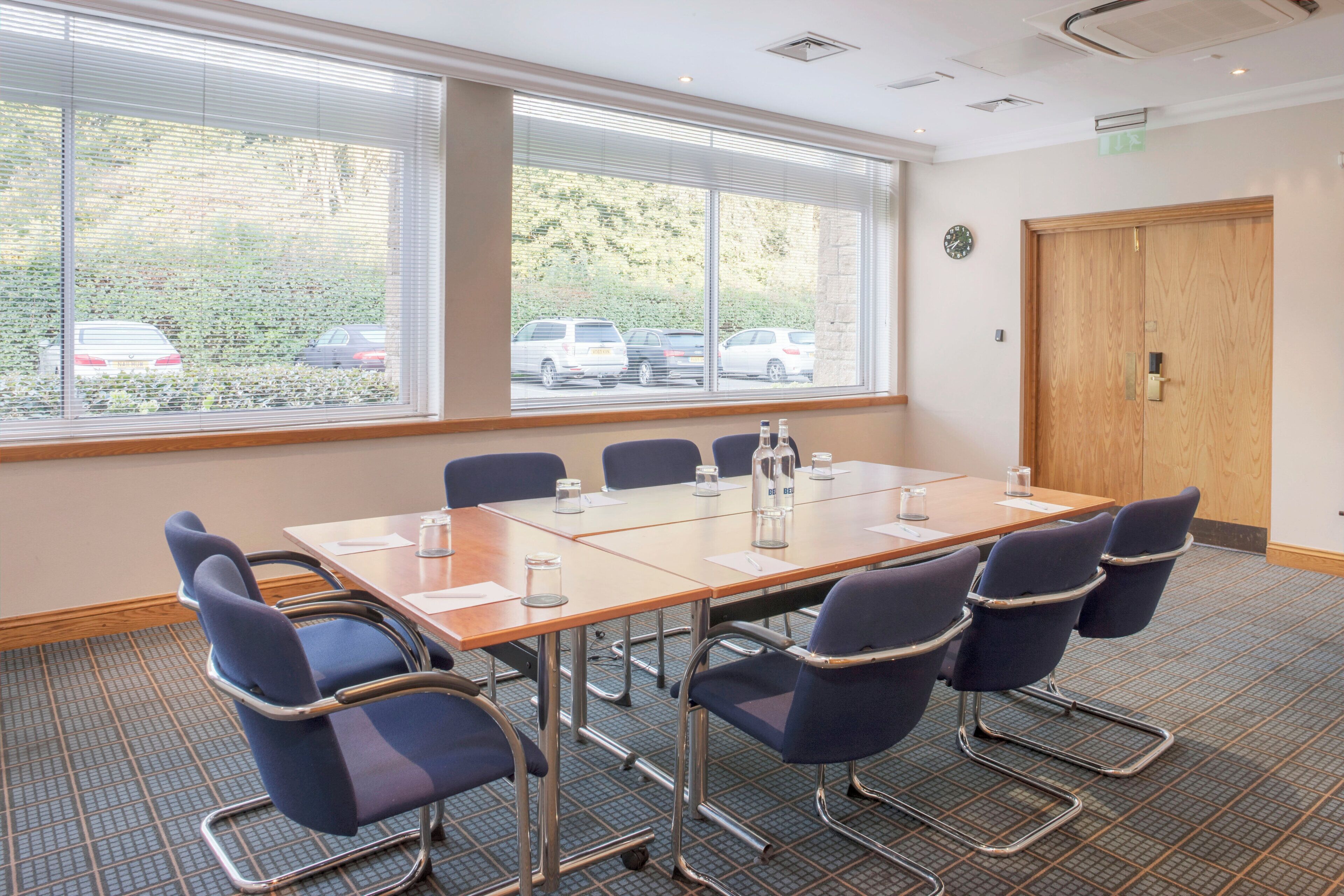 A conference room with a large table, six chairs, and a view of parked cars through the windows.