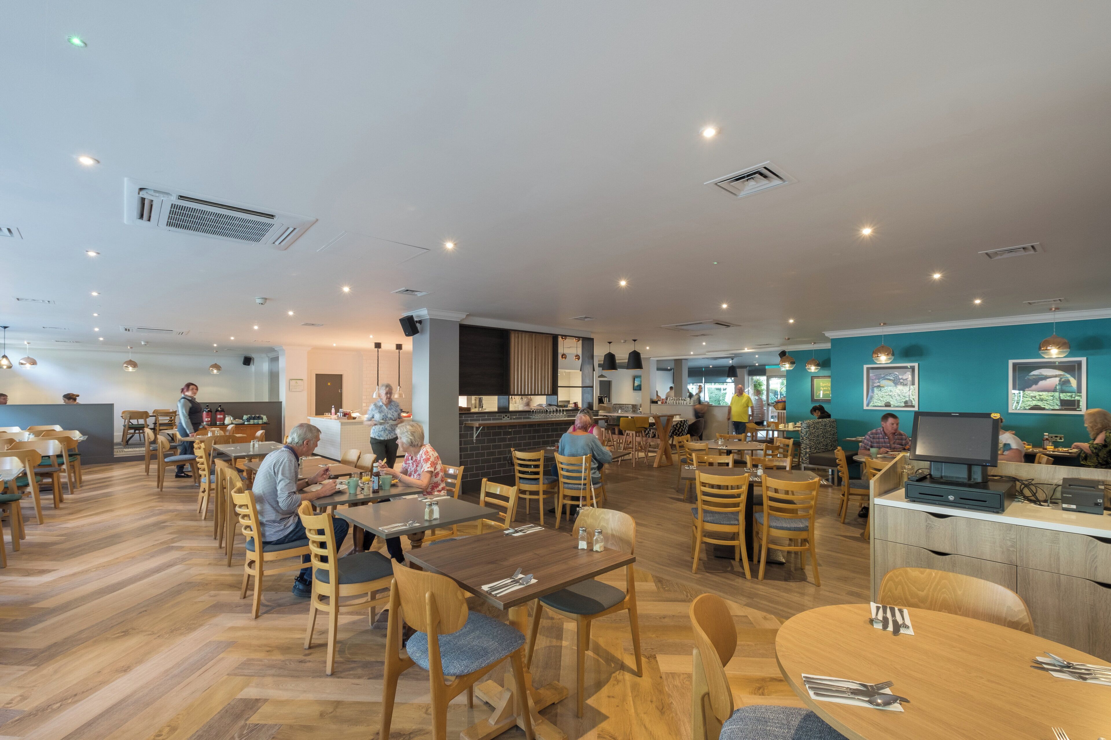 Un restaurante espacioso con varias zonas de comedor, mobiliario de madera y una barra.