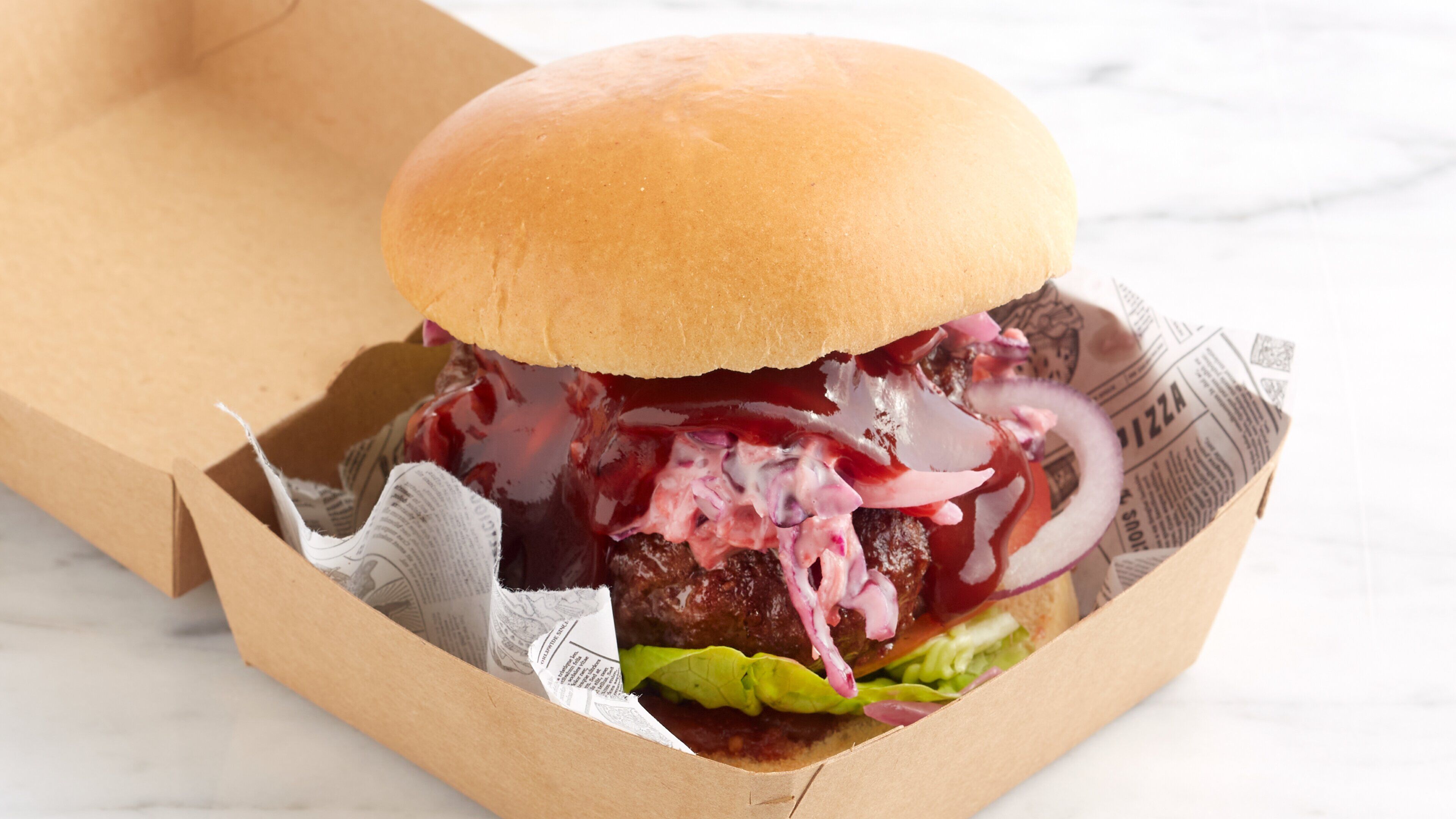 A burger in a paper container with lettuce, red onion, and a sauce.