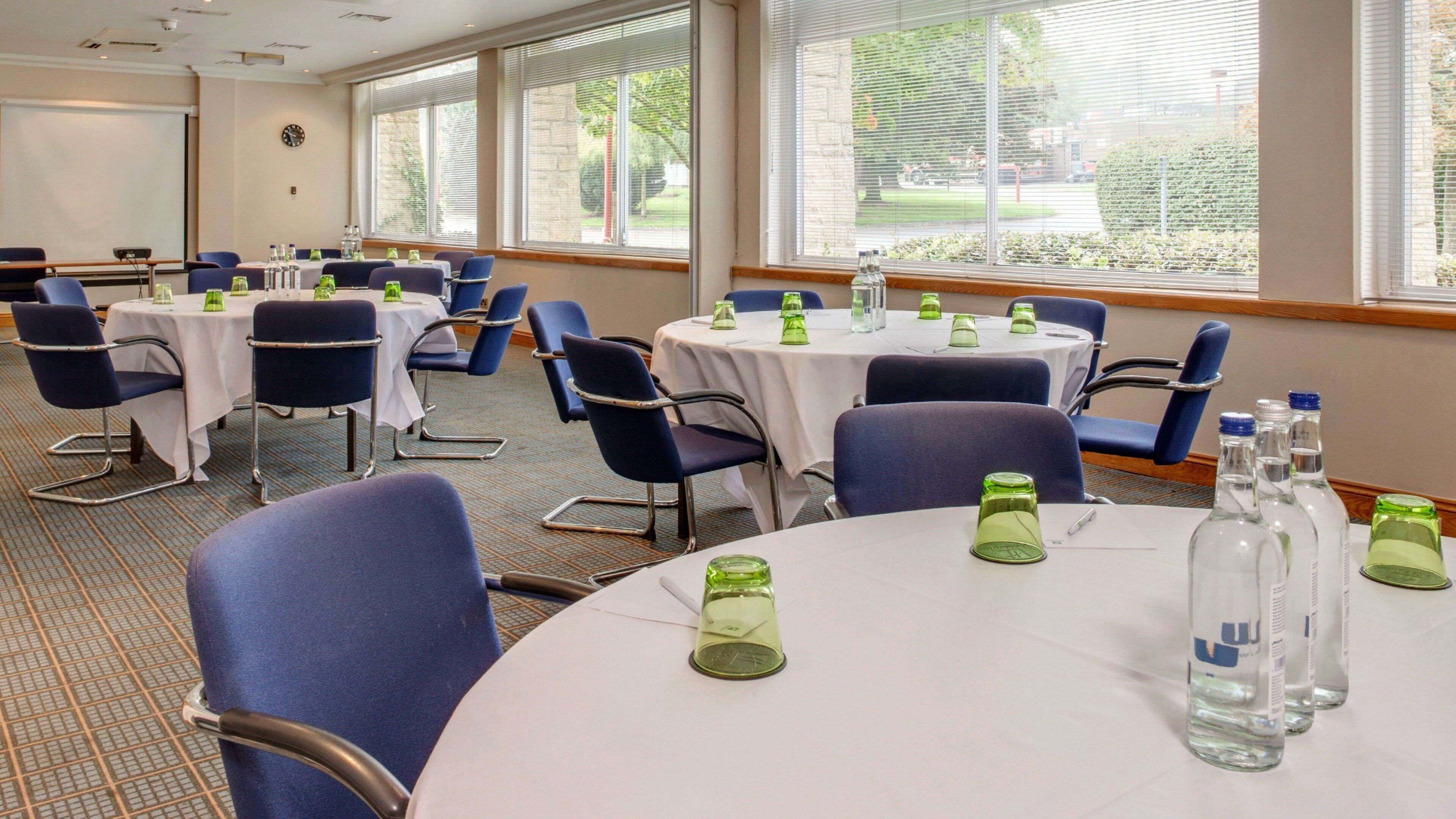 A conference room with round tables, chairs, and green glass candle holders.