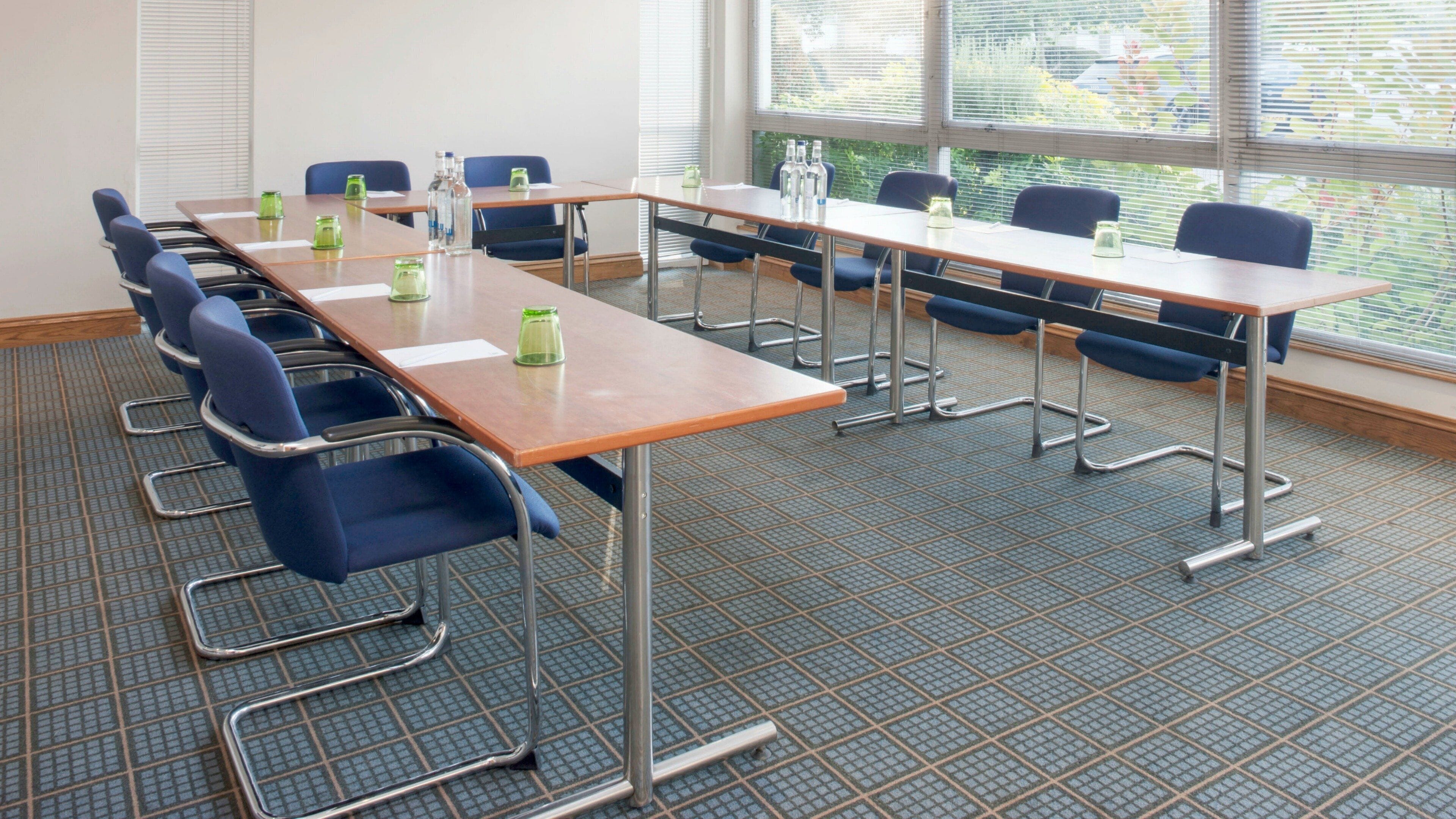A conference room with a long table, blue chairs, and a grid-patterned floor.