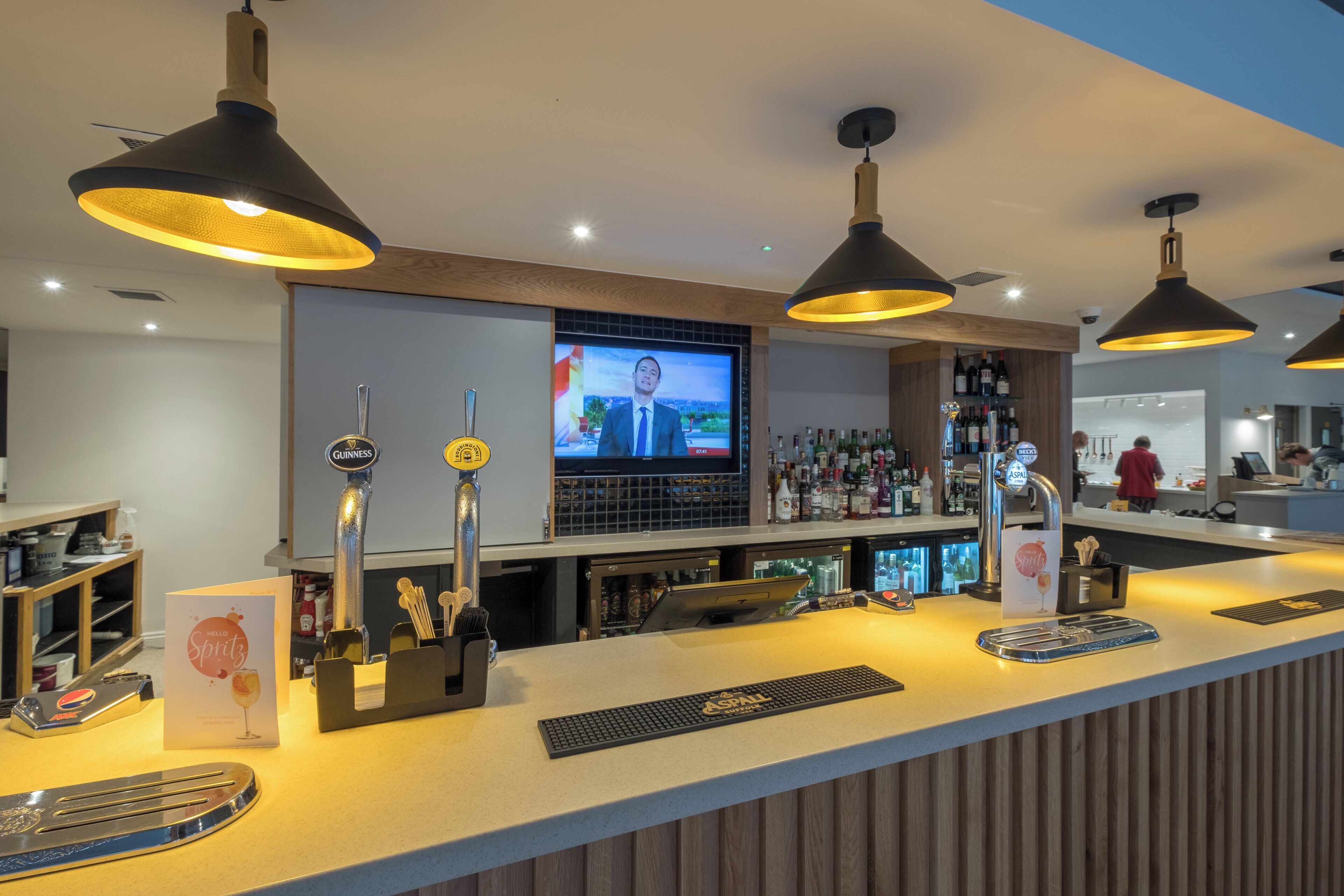 Uma área de bar com várias torneiras, uma tela de televisão e uma seleção variada de garrafas.