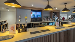 A bar area with multiple taps, a television screen, and a variety of bottles. - Holiday Inn Swindon by IHG (Swindon)